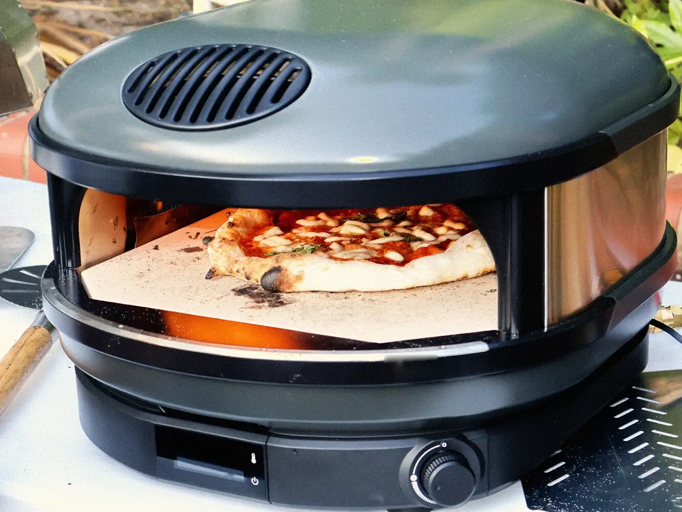 A margherita part-baked on the stone inside the oven, the chamber glowing behind it, the rig set up outdoors